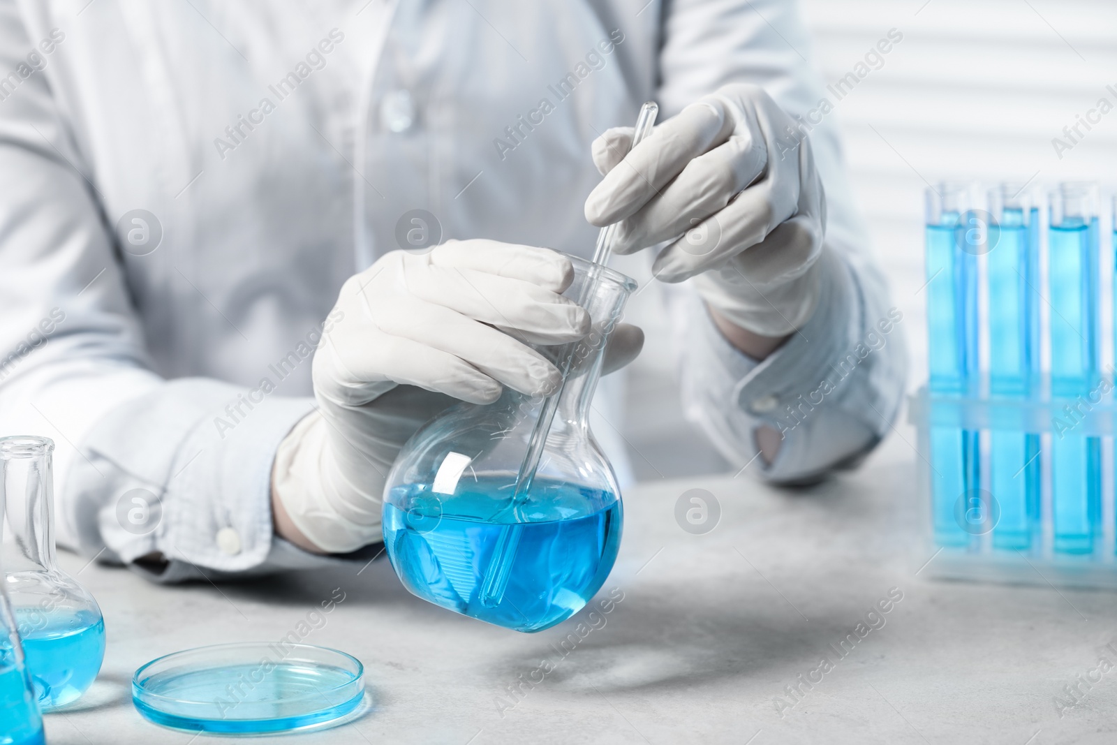 Photo of Scientist taking sample of light blue liquid at white table in laboratory, closeup