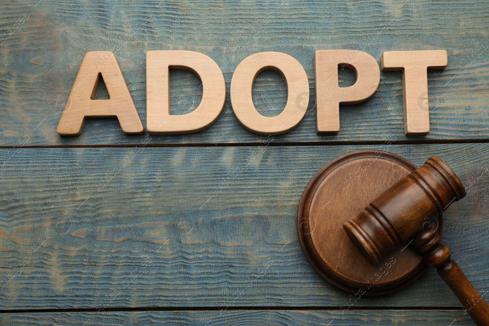 Photo of Word Adopt and gavel on blue wooden table, flat lay