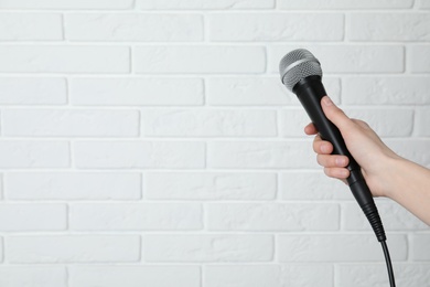 Photo of Woman holding modern microphone near brick wall, closeup. Space for text