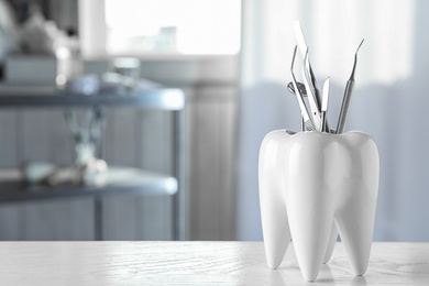 Photo of Tooth shaped holder with professional dentist tools on table in clinic. Space for text