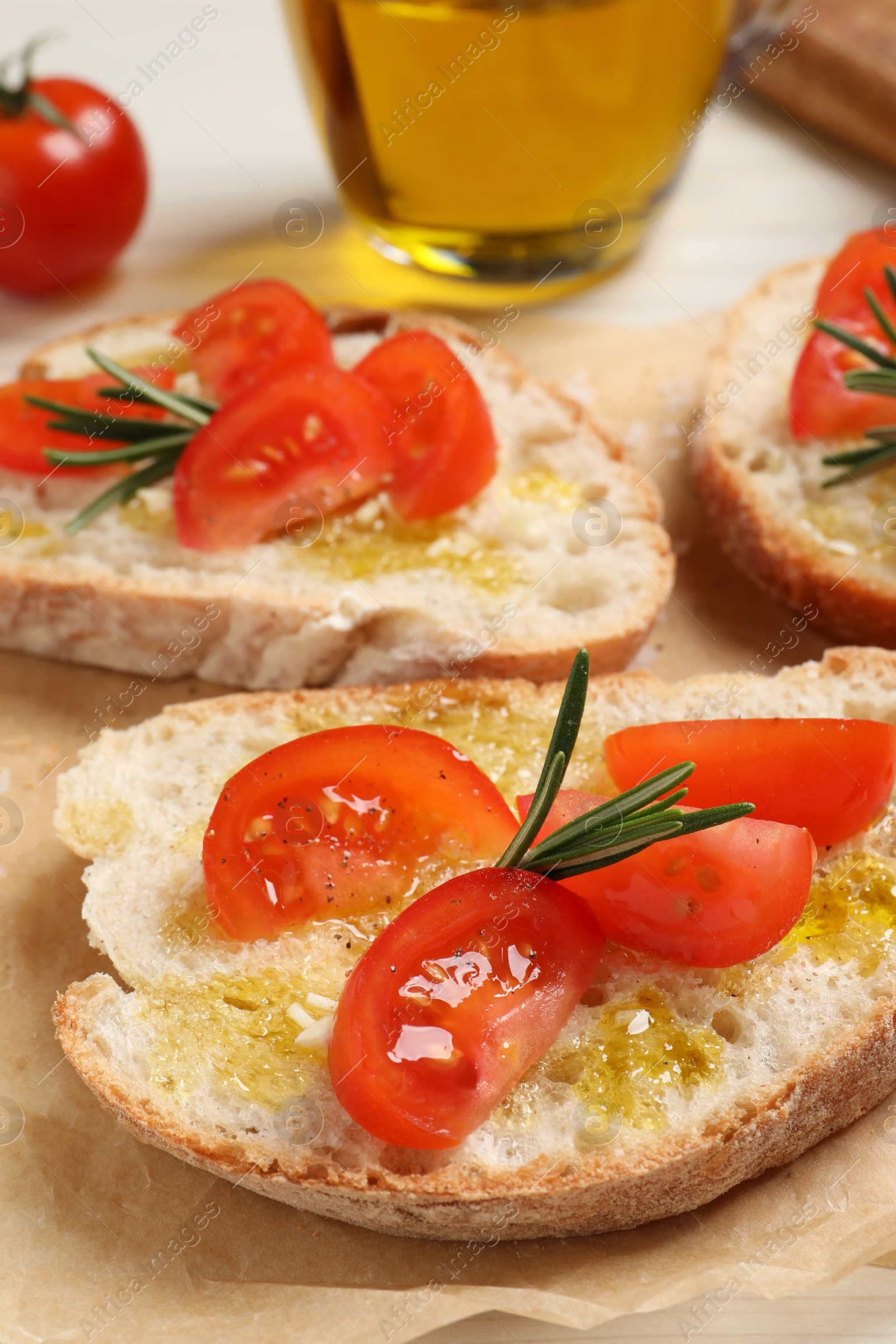 Photo of Tasty bruschettas with oil, tomatoes and rosemary on parchment paper, closeup