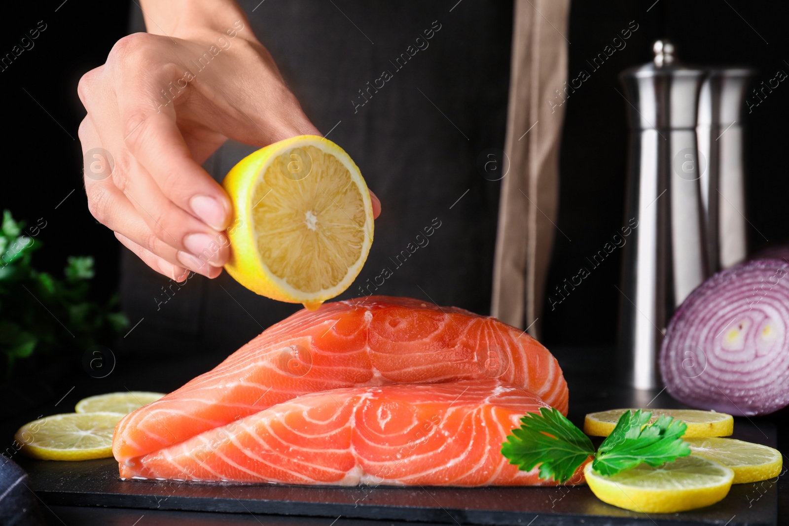 Photo of Woman squeezing lemon onto fresh raw salmon at table, closeup. Fish delicacy