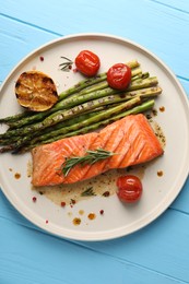 Photo of Tasty grilled salmon with asparagus, tomatoes and spices on light blue wooden table, top view