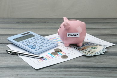 Photo of Piggy bank with word Pension, dollar banknotes, coins, pen, calculator and diagrams on grey wooden table. Retirement savings