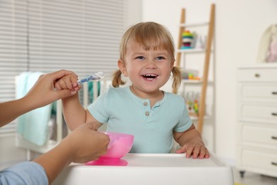 Mother feeding her cute little child with yogurt at home