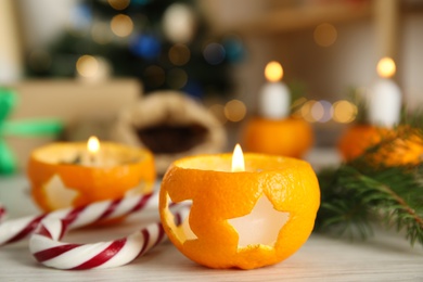 Photo of Burning candle in tangerine peel as holder on white wooden table