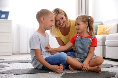 Photo of Happy mother playing with her children on floor at home