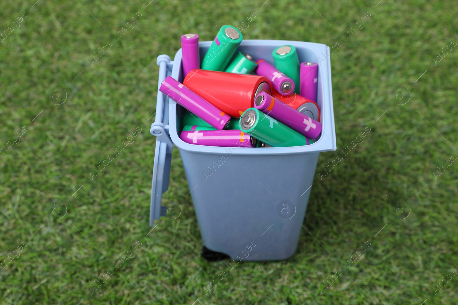 Photo of Many used batteries in recycling bin on green grass