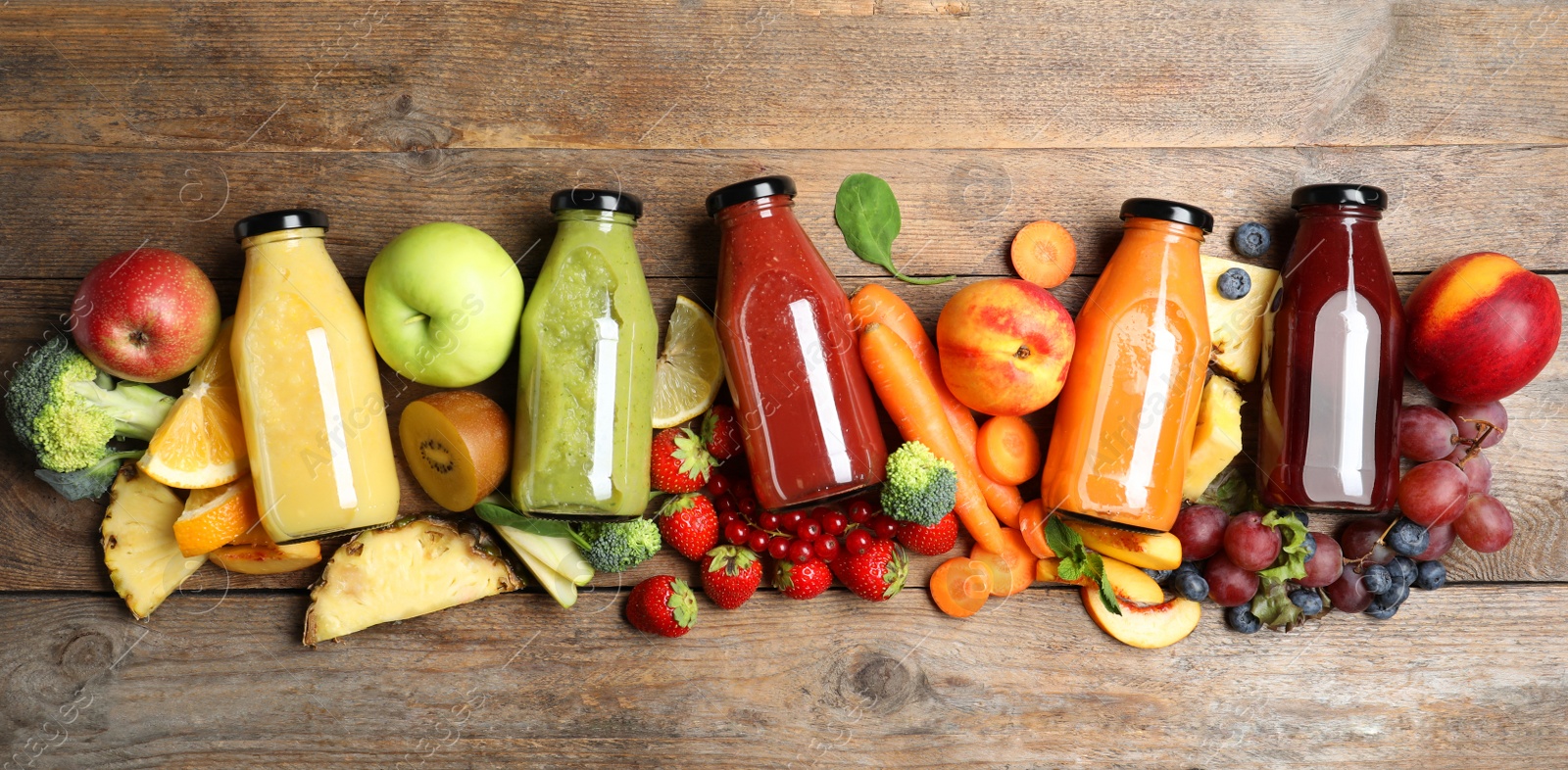 Photo of Bottles of delicious juices and fresh fruits on wooden table, flat lay