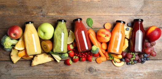 Photo of Bottles of delicious juices and fresh fruits on wooden table, flat lay