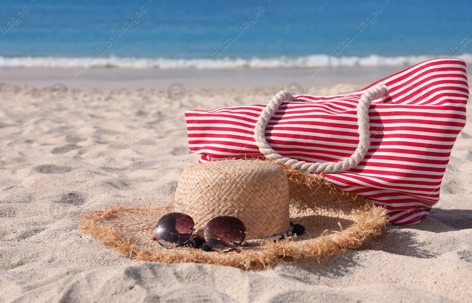 Photo of Straw hat with sunglasses and bag on sandy beach