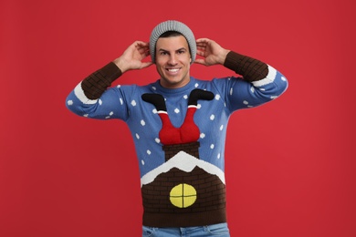 Happy man in Christmas sweater and hat on red background