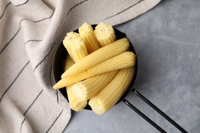 Tasty fresh yellow baby corns in dish on grey table, top view