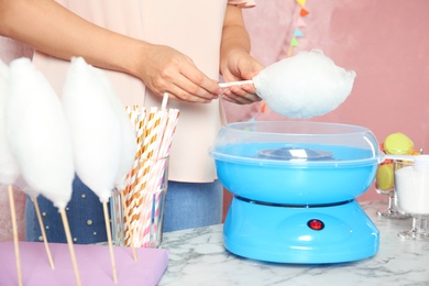 Woman making cotton candy using modern machine at table, closeup