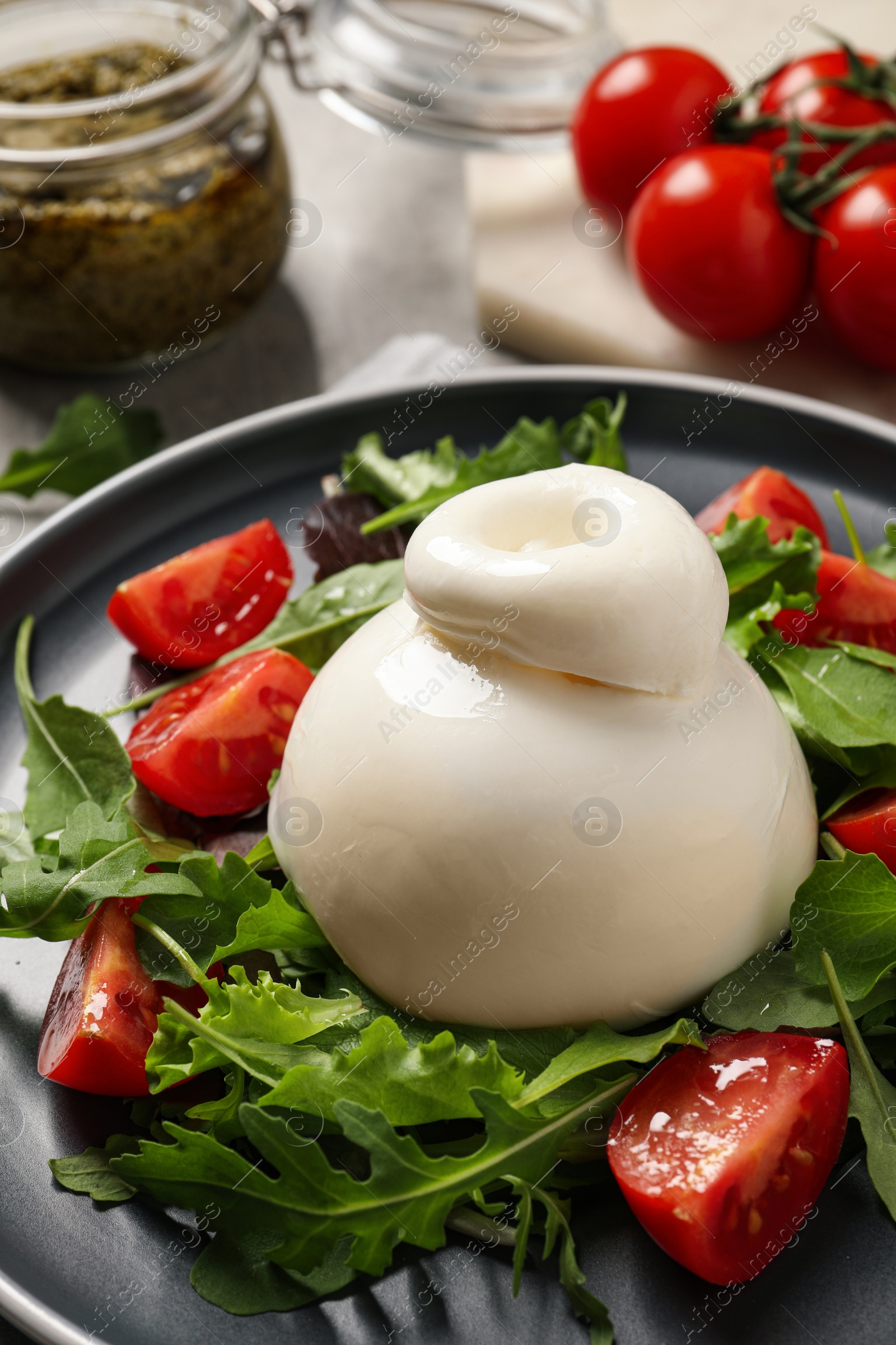 Photo of Delicious burrata salad with tomatoes and arugula on table, closeup