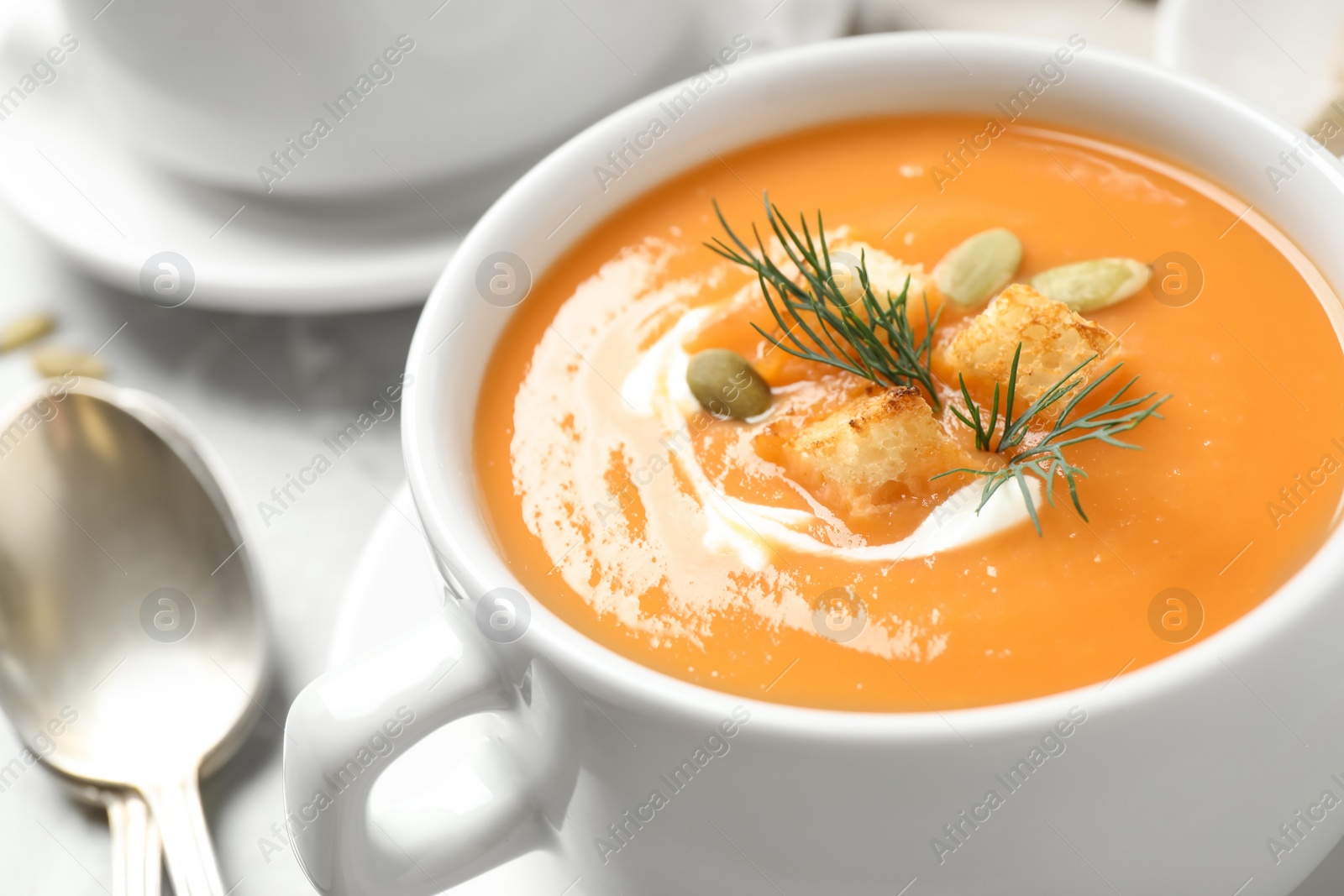 Photo of Tasty creamy pumpkin soup with croutons, seeds and dill in bowl on table, closeup