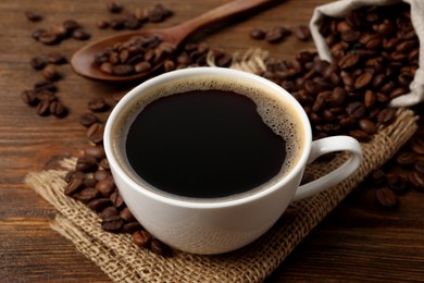 Photo of Cup of aromatic hot coffee and beans on wooden table