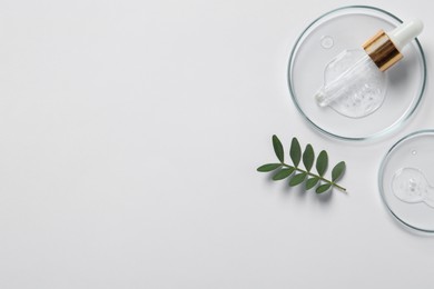 Photo of Petri dishes with samples of cosmetic oil, pipette and green leaves on white background, flat lay. Space for text