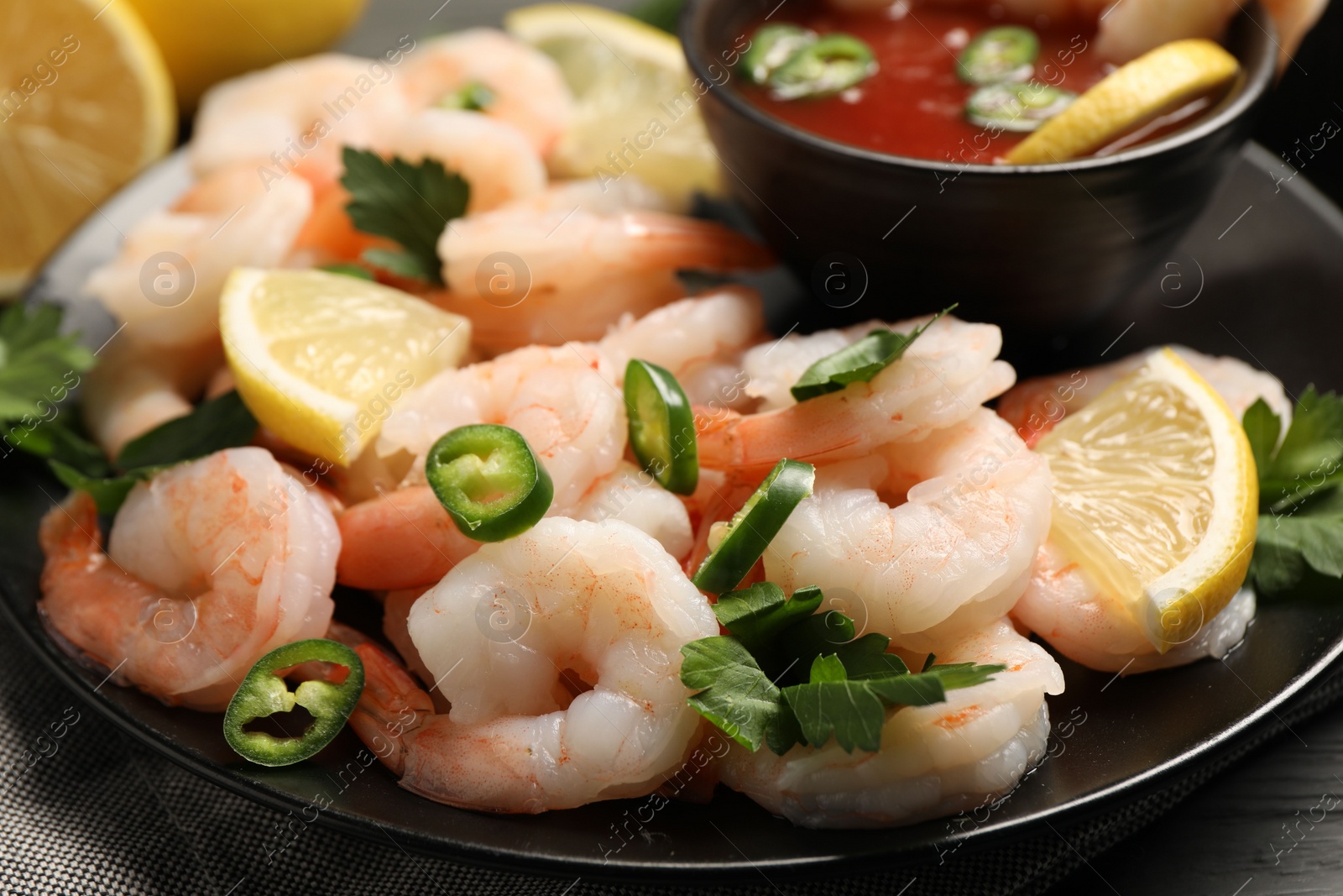 Photo of Tasty boiled shrimps with cocktail sauce, chili, parsley and lemon on table, closeup