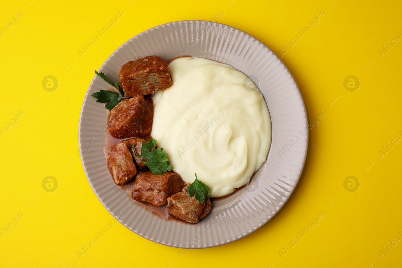 Photo of Delicious goulash with mashed potato on yellow background, top view