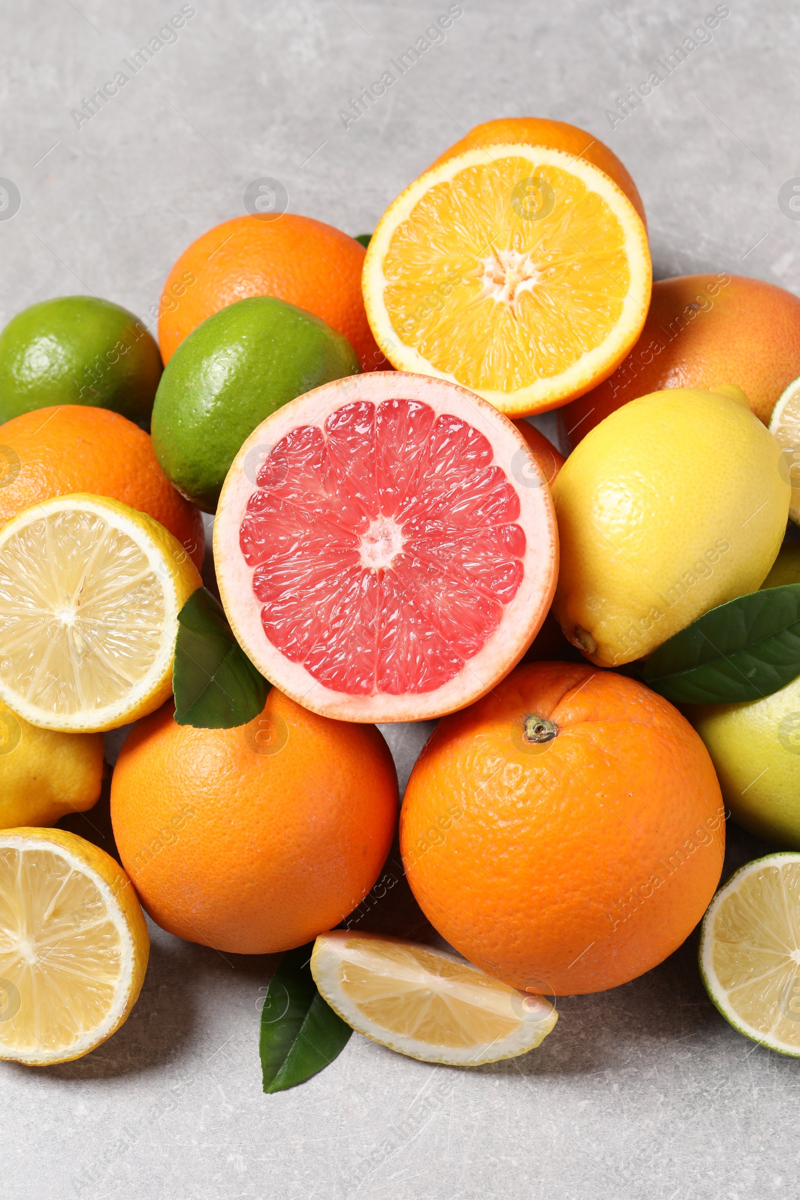 Photo of Pile of different fresh citrus fruits and leaves on grey textured table