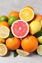 Pile of different fresh citrus fruits and leaves on grey textured table