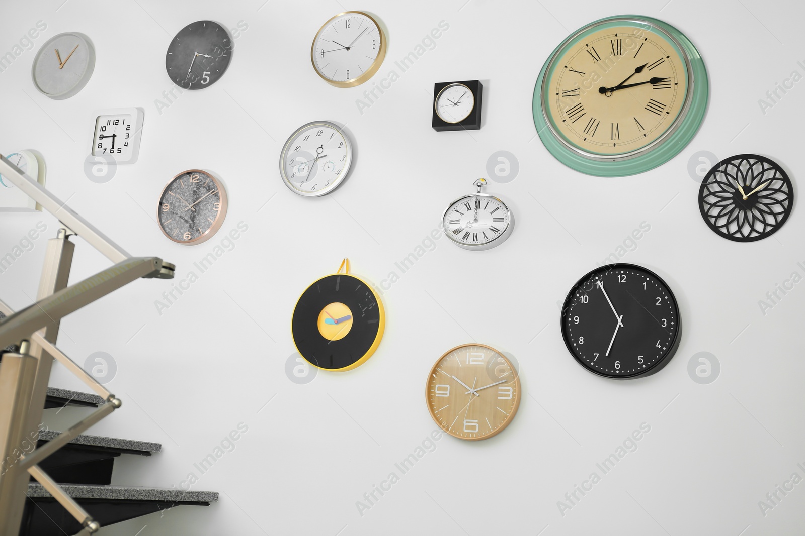 Photo of Many different clocks hanging on white wall. Time of day