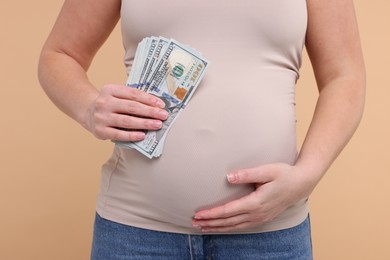 Photo of Surrogate mother. Pregnant woman with dollar banknotes on beige background, closeup