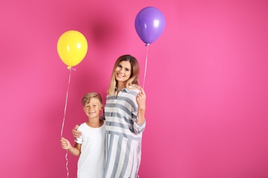 Mother and son with balloons on color background