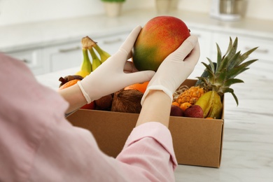 Woman with assortment of exotic fruits at table in kitchen, closeup