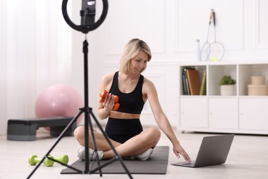 Smiling sports blogger with dumbbells streaming online fitness lesson with phone at home