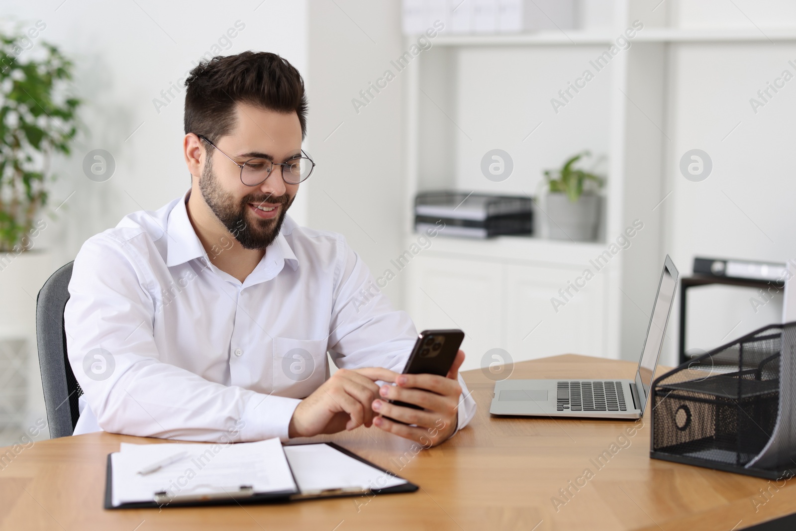 Photo of Handsome young man using smartphone at wooden table in office