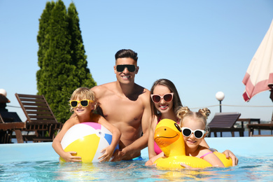 Happy family with inflatable ring and ball in outdoor swimming pool on sunny summer day