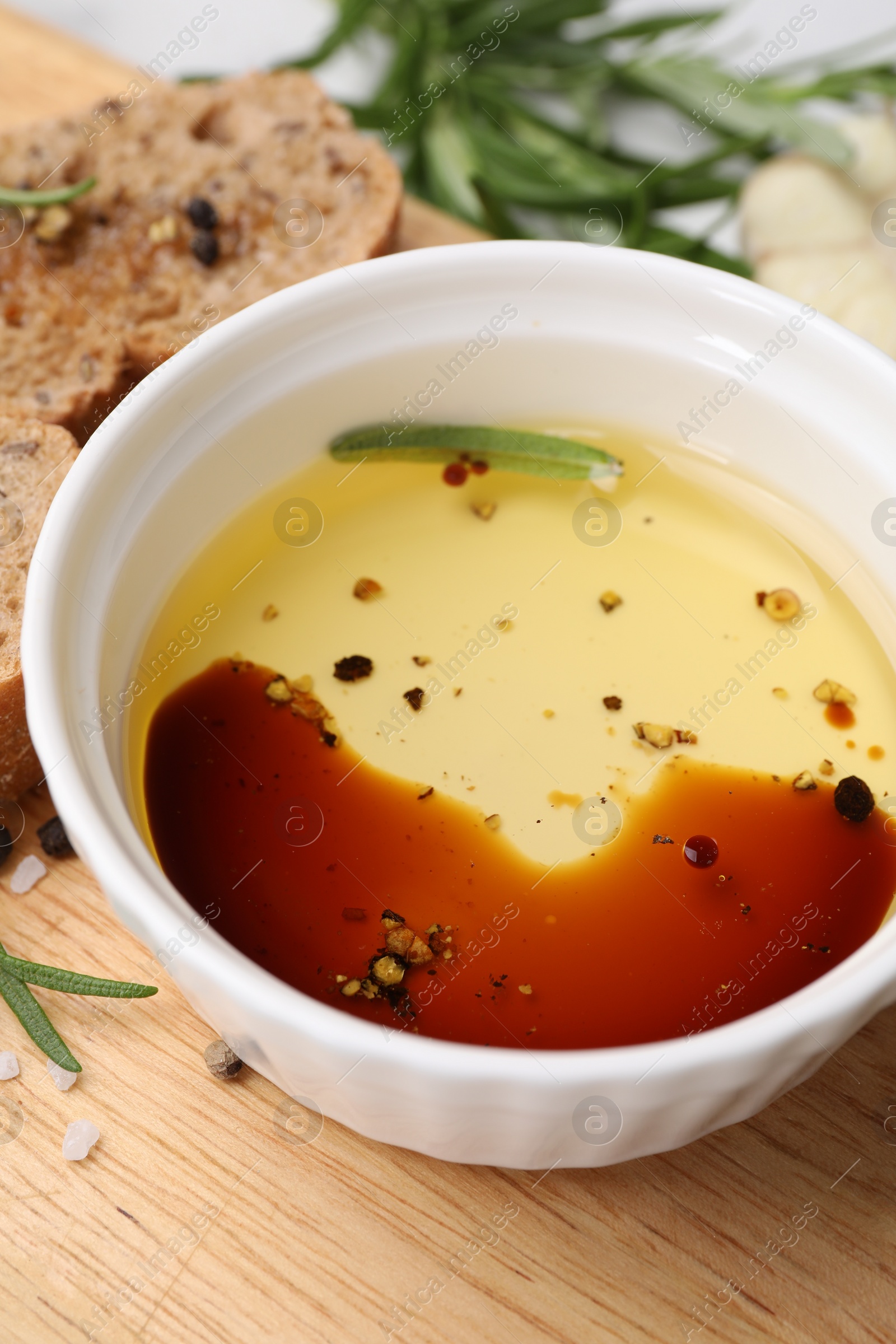 Photo of Bowl of organic balsamic vinegar with oil, bread slices and spices on wooden board, closeup