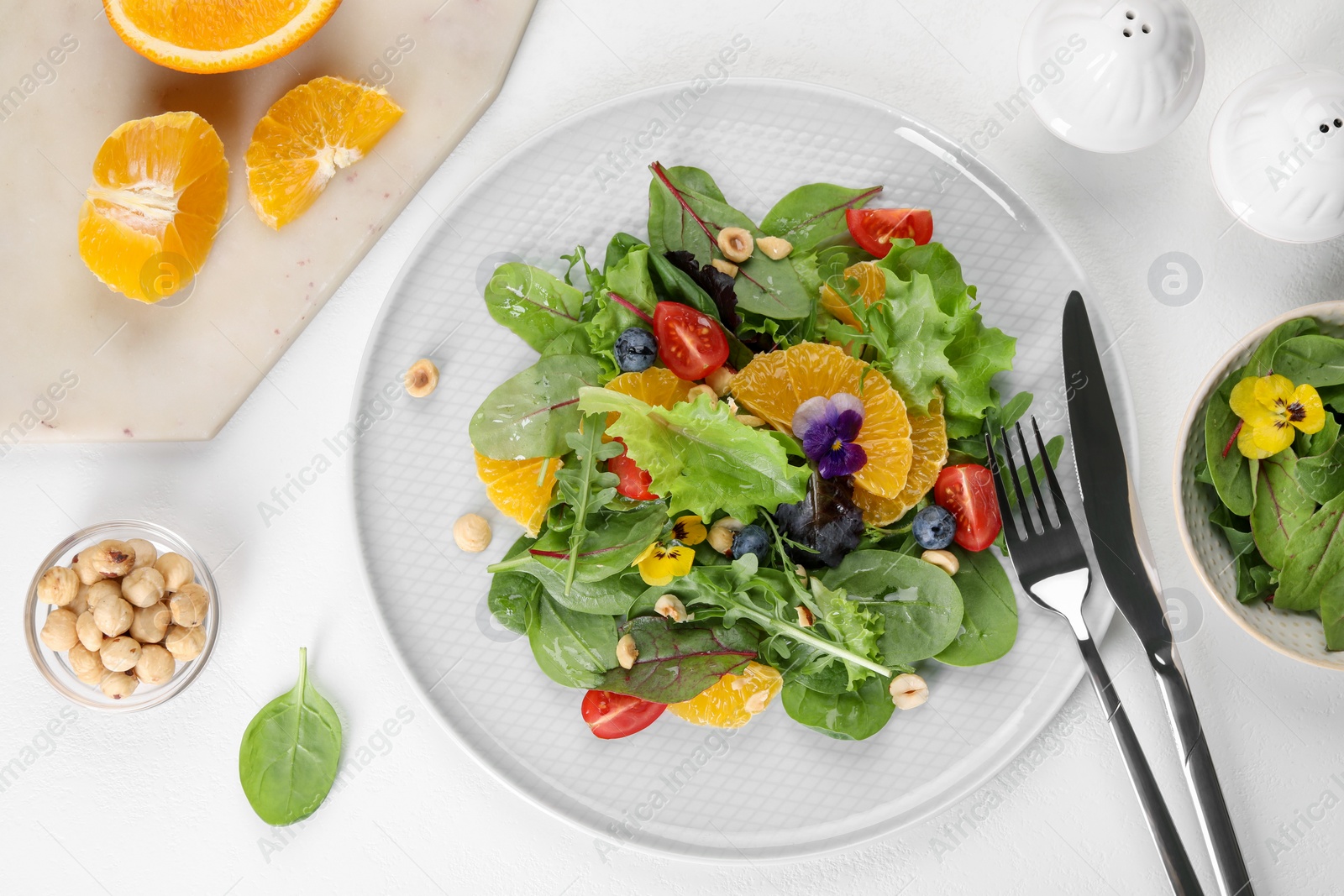 Photo of Delicious salad, ingredients and cutlery on white table, flat lay