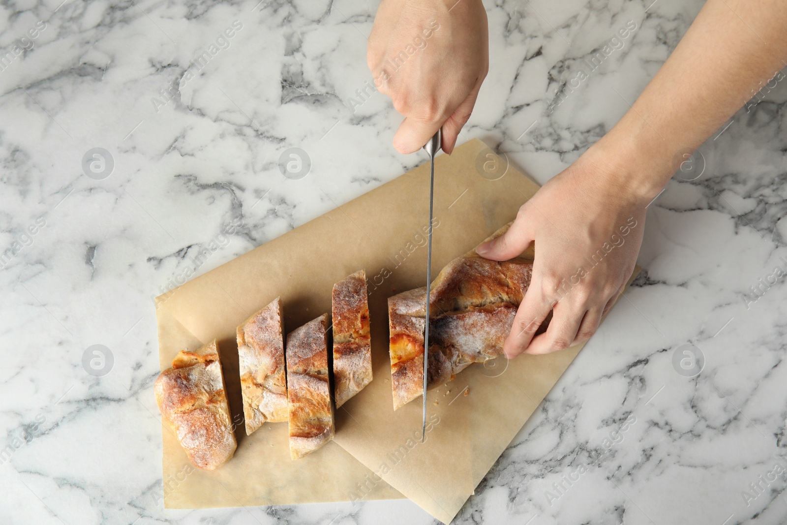 Photo of Woman cutting bread on marble background, top view