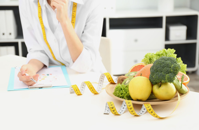Photo of Nutritionist at desk with fruits, vegetables and measuring tape in clinic, closeup