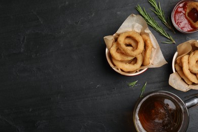 Photo of Fried onion rings served on black table, flat lay. Space for text