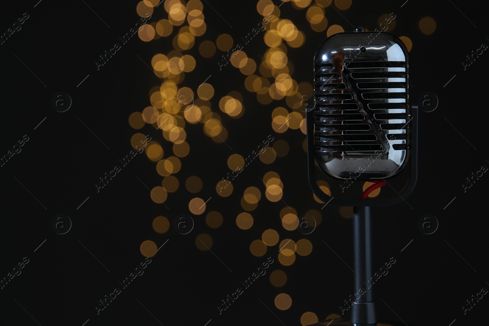 Photo of Sound recording and reinforcement. Vintage microphone against black background with blurred lights, closeup. Space for text