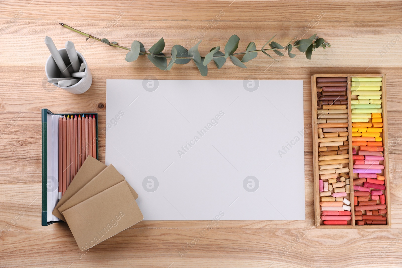 Photo of Layout with blank paper, soft pastels and other drawing supplies on wooden table at artist's workplace, top view. Space for design