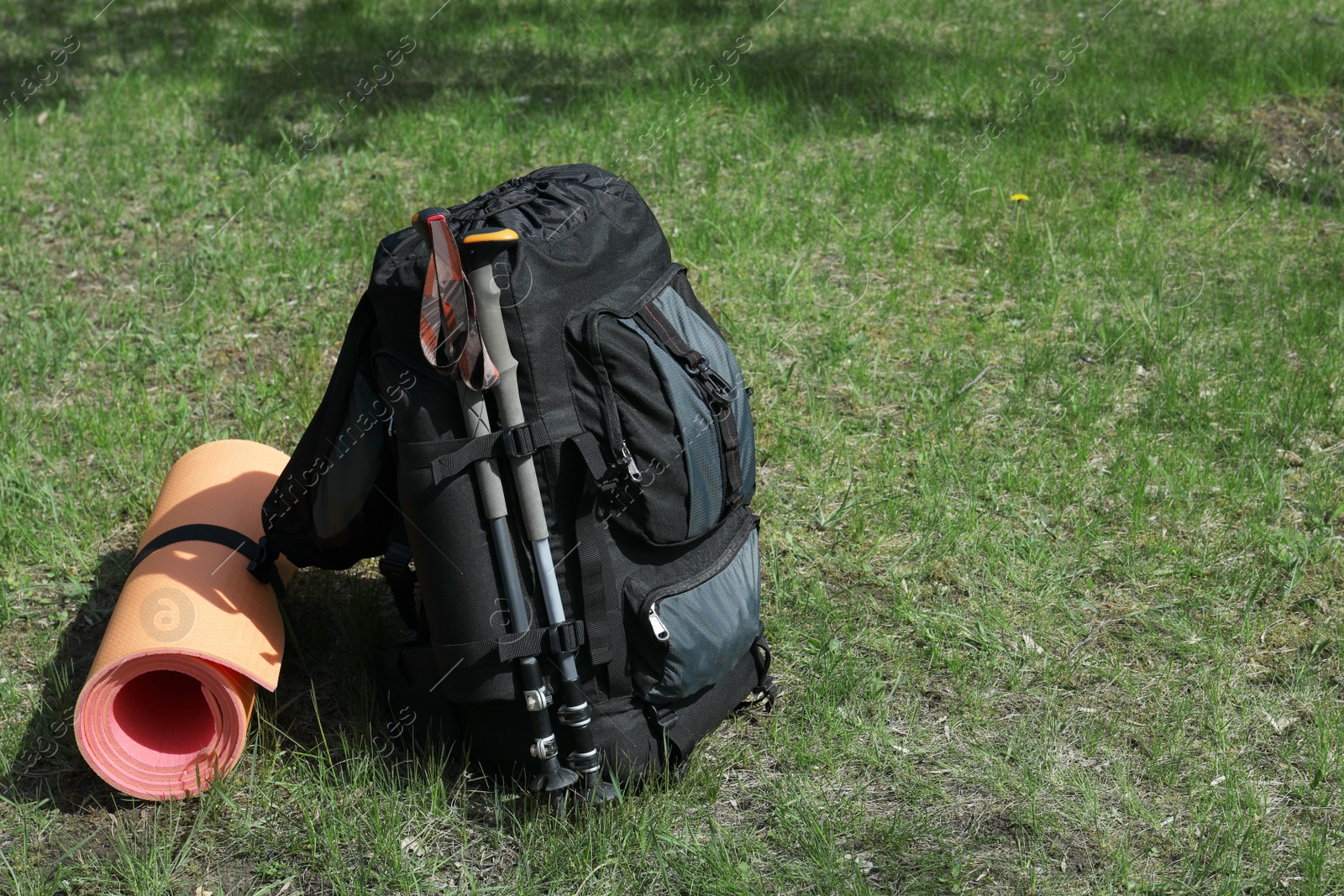 Photo of Backpack with trekking poles and camping mat on green grass. Space for text