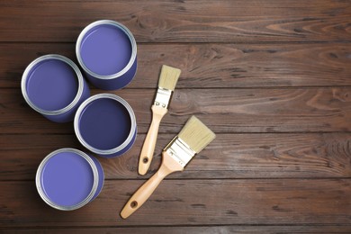 Image of Cans with violet paints and brushes on wooden background, top view. Space for text
