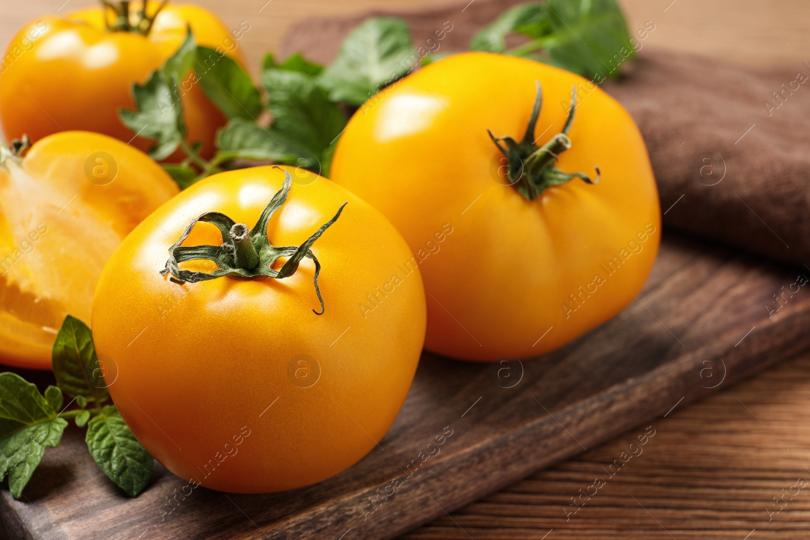 Photo of Fresh ripe yellow tomatoes with leaves on wooden table, closeup