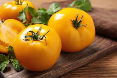 Fresh ripe yellow tomatoes with leaves on wooden table, closeup