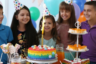 Happy children near cake with firework candle at birthday party indoors