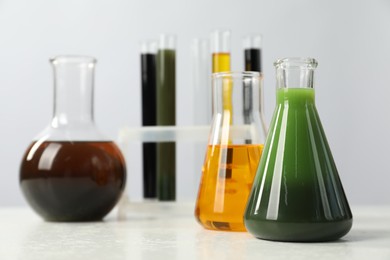 Photo of Laboratory glassware with different types of oil on white table, closeup