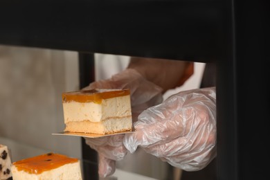 Photo of Worker taking tasty piece of cheesecake with jelly from showcase in cafe, closeup