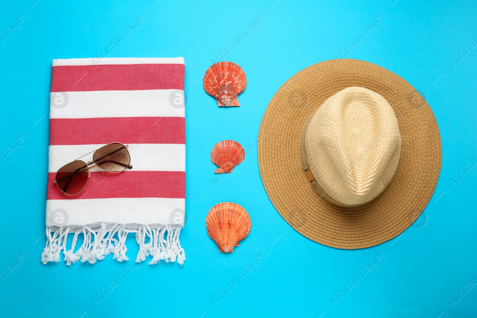 Photo of Beach towel, sunglasses and straw hat on light blue background, flat lay