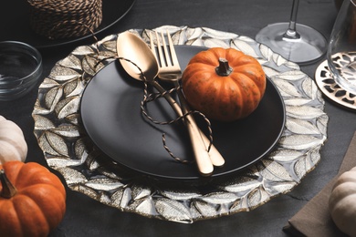 Autumn table setting with golden cutlery and pumpkin on black background