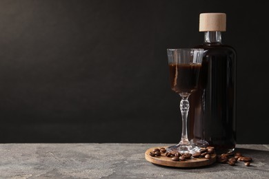 Photo of Bottle of coffee liqueur, shot glass and beans on light grey table, space for text